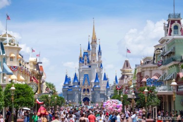 Iconic Disney castle with blue turrets and golden spire at Magic Kingdom, surrounded by visitors and.